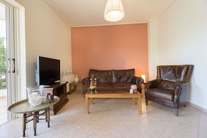 A living room with a television, leather sofa, armchair, coffee table, and decorative items.