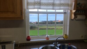A kitchen with a window view of a green landscape and the sea. - PICO Hollidays  Rentals- Mountain and sea view for families or  groups (São Roque do Pico)