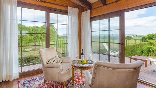 A room with large windows, a wooden ceiling, and a table with a bottle and glasses.