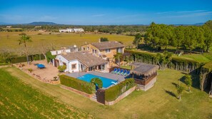 Una casa grande con piscina, un porche cubierto y vistas al campo circundante.