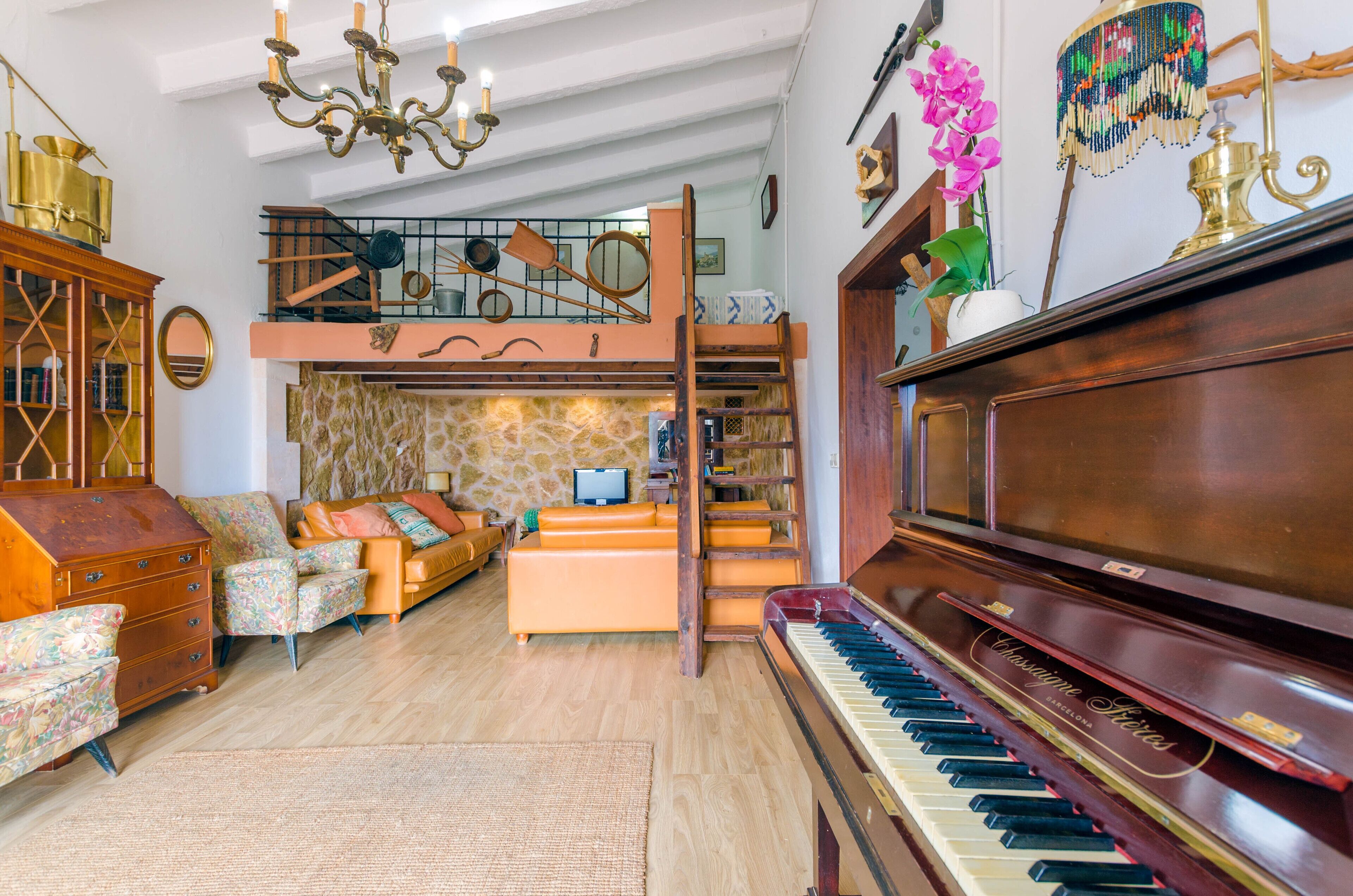 Un vaste salon agrémenté d’un magnifique piano à queue, d’un confortable ensemble de canapés, d’un escalier en bois et d’un plafond haut orné de lustres.
