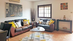 A living room with a sofa set, a coffee table, a large window, and a painting on the wall. - Three double bedroom townhouse in lovely village (San Javier, Murcia)