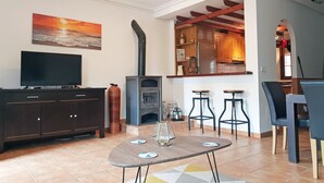 A living room with a TV, a fireplace, a dining area with bar stools, and a kitchen visible through an archway. - Three double bedroom townhouse in lovely village (San Javier, Murcia)