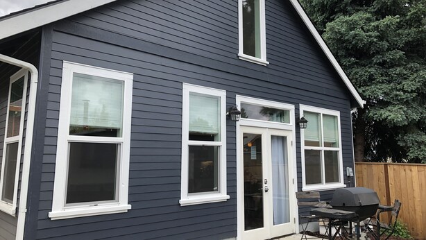 A two-story house with a dark exterior, white trim, and multiple windows.