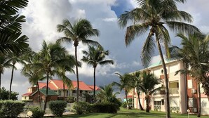 A hotel with a red roof, surrounded by palm trees and a well-maintained lawn. - Ti Treasure Apartment Ground Floor T3 Crystal Beach (Saint-François)
