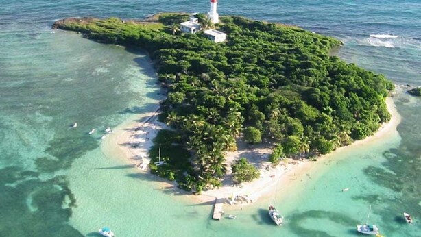An aerial view of a small island with a lighthouse, surrounded by clear turquoise waters and dense green vegetation. - Ti Treasure Apartment Ground Floor T3 Crystal Beach (Saint-François)