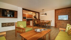 Un salón acogedor con una mesa de comedor de madera, sofá verde estampado y una cocina al fondo.