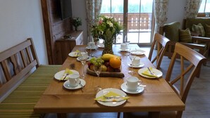 Una mesa de comedor dispuesta con platos, cubiertos y una cesta de frutas.