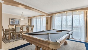 Une table de billard dans une pièce comprenant un coin repas, de grandes fenêtres et une vue sur l’extérieur.