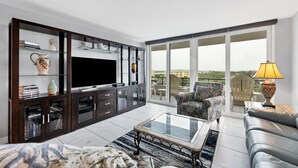 Ein modernes Wohnzimmer mit Flachbildfernseher, einer Unterhaltungsmöbel aus dunklem Holz, einem Glastisch und Blick auf die Stadt durch große Fenster.