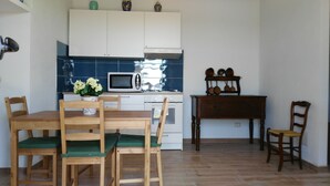 A small kitchen with white cabinets, a microwave, and a stove. There is a dining table with chairs and a vase of flowers. - New!Peonia house in the mountains wonderful panorama (Sardinia) Last minute!26Lug-2LtCl (Seulo)