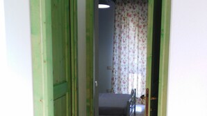 A narrow hallway with green-painted doors leading to a room with a bed and floral curtains. - New!Peonia house in the mountains wonderful panorama (Sardinia) Last minute!26Lug-2LtCl (Seulo)