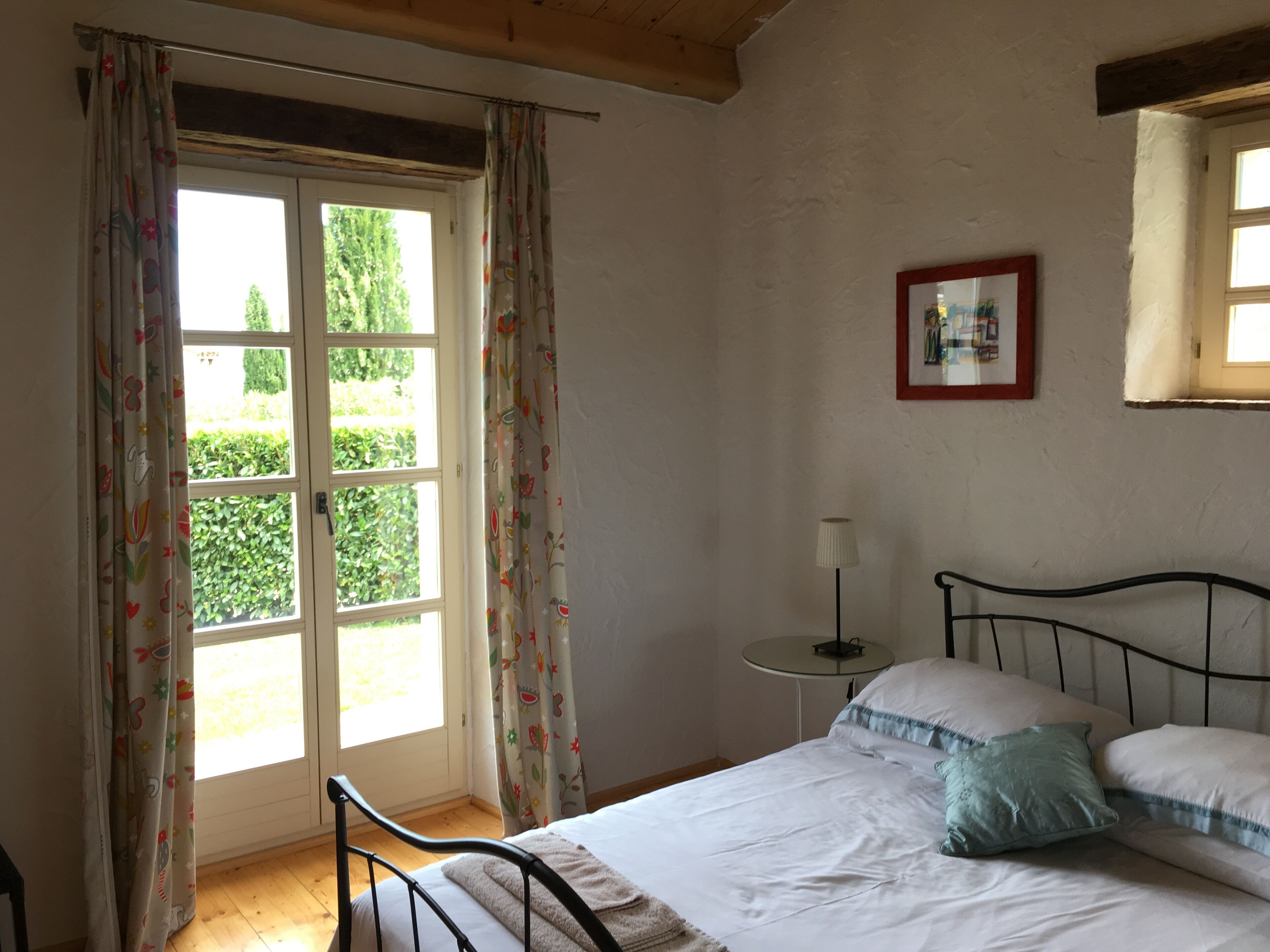 A bedroom with a bed, a bedside table, a lamp, and a window with curtains.
