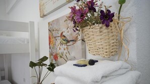 Een badkamer met een witte badkuip, een rieten mand met bloemen, een ingelijst bloemig kunstwerk en een kleine potplant.
