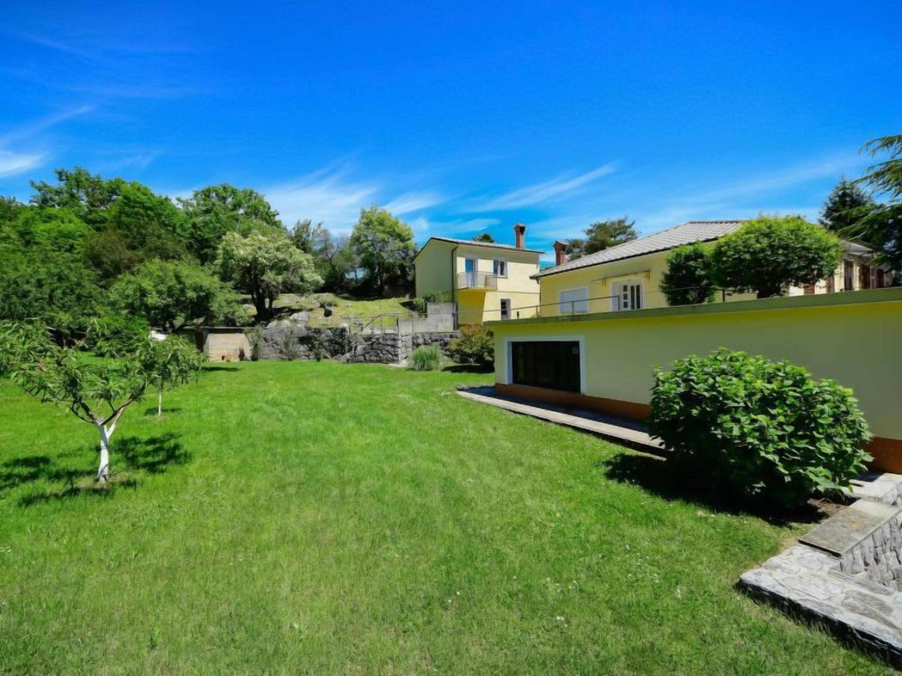 A residential property with a well-maintained lawn, a stone wall, and a yellow building with a garage.