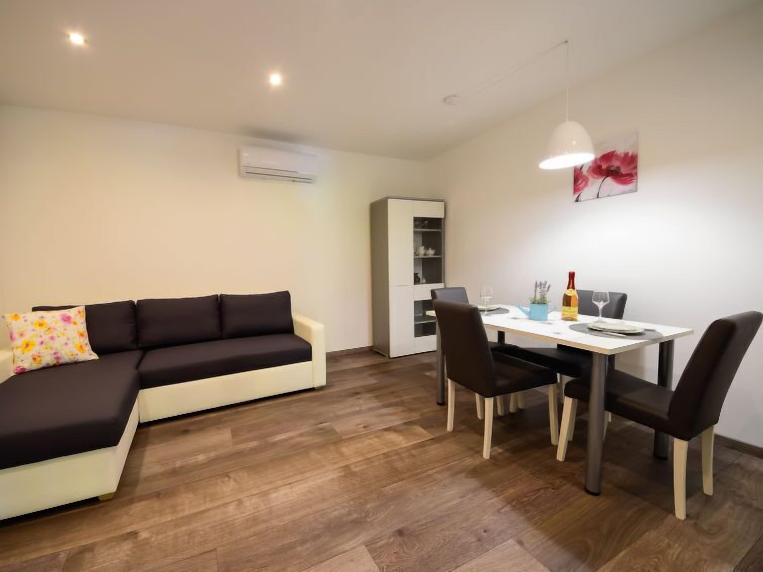 A modern living room with a sectional sofa, a dining table with chairs, a cabinet, and a painting on the wall.