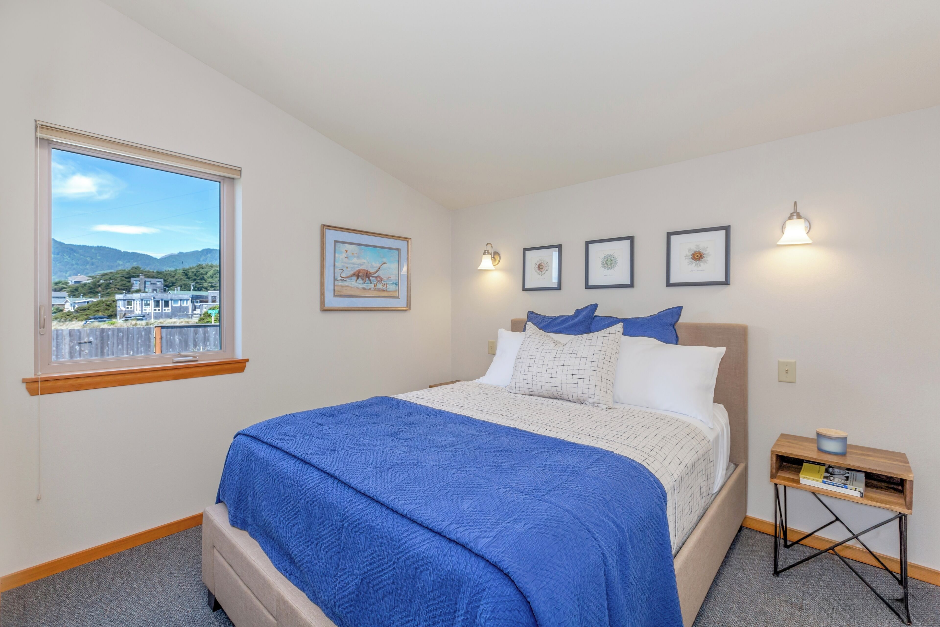 A bedroom with a large bed, a window with a view of buildings and mountains, and three framed pictures on the wall.