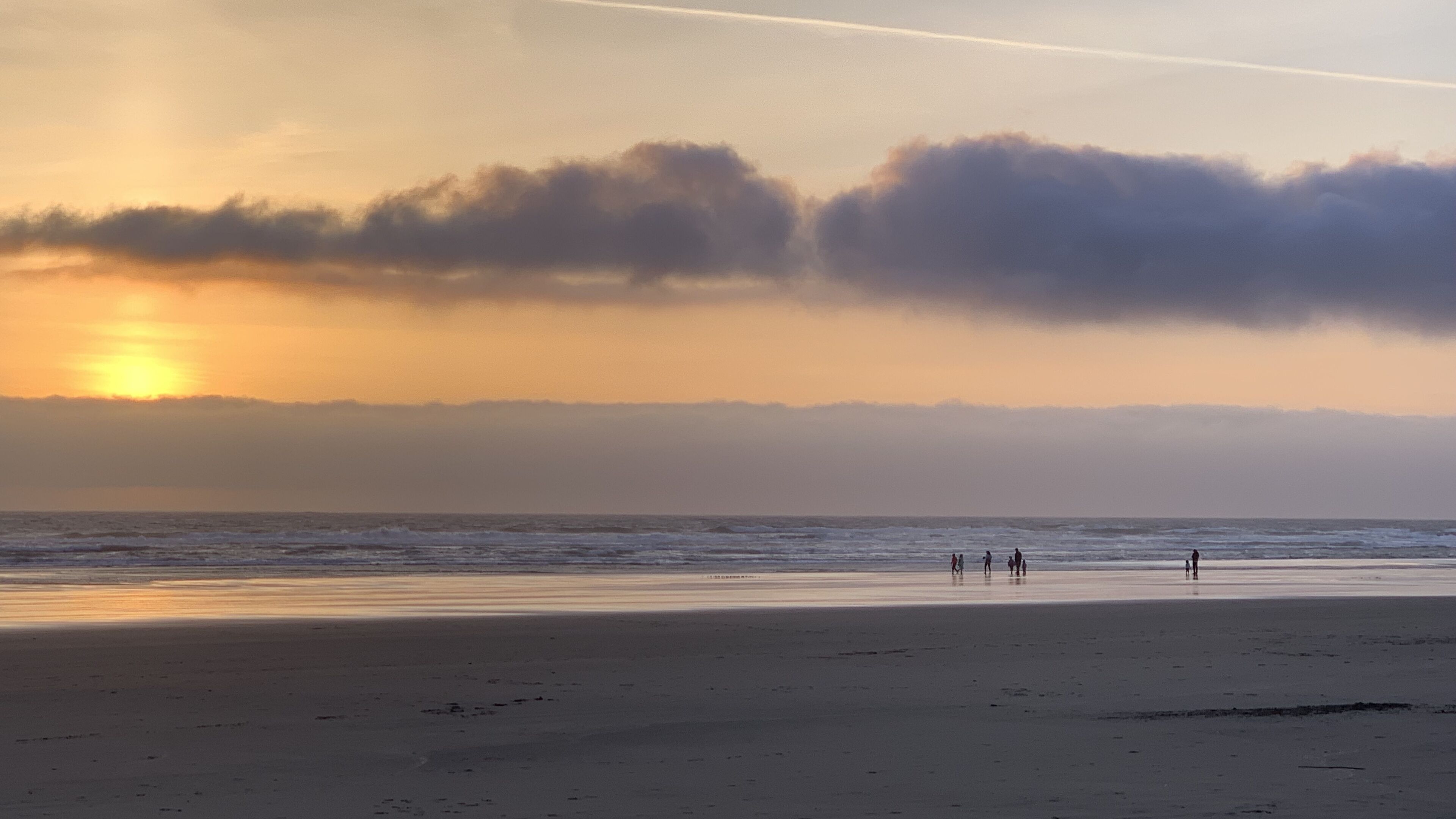 Une plage où des personnes se promènent le long du rivage au coucher du soleil.