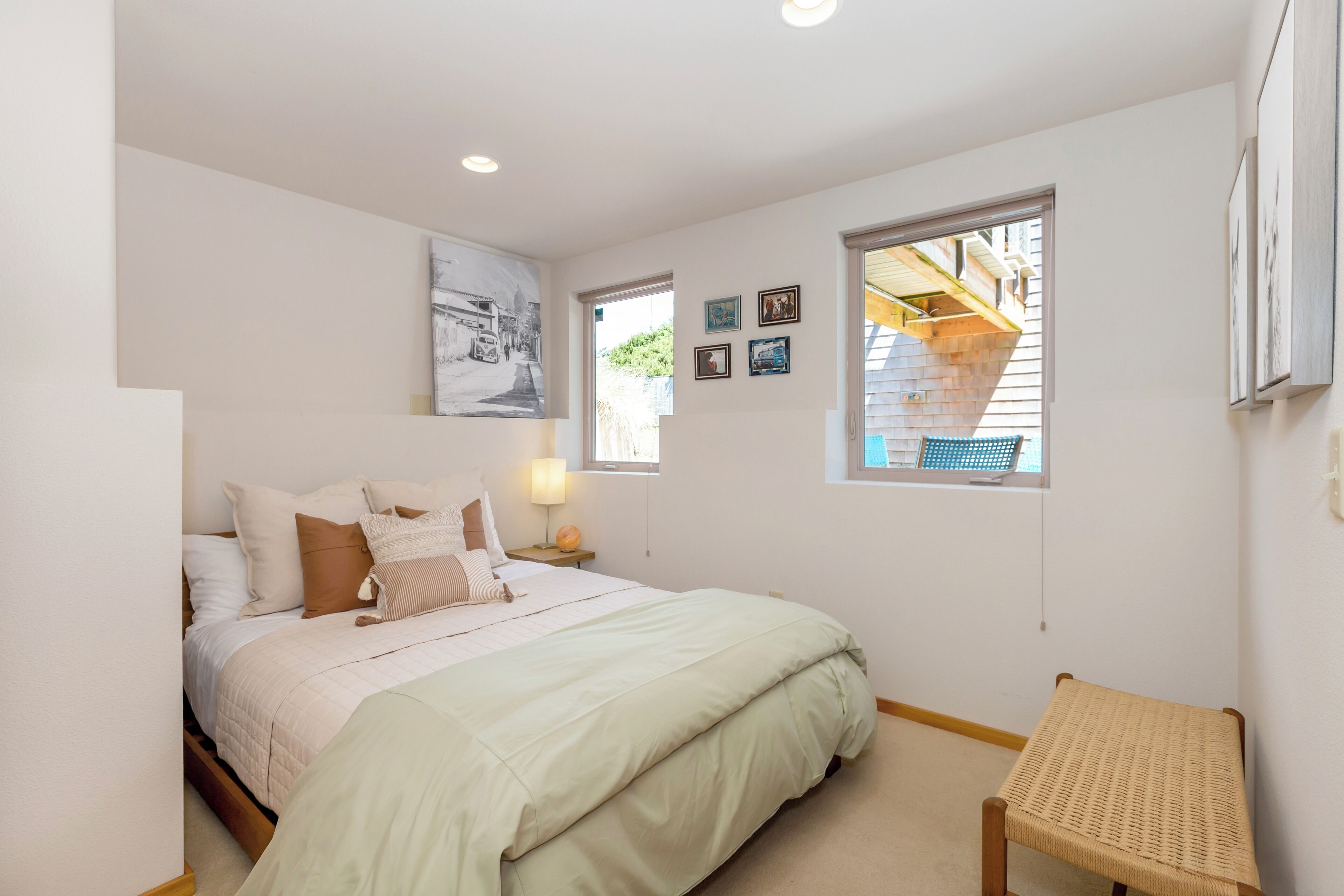 A bedroom with a bed, a bedside table, a chair, and a window with a view of the outside.