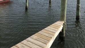 A wooden dock extending into calm water with a red boat docked on the left. - In The Heart of Hatteras Village. Close to Beach, Restaurants and Marinas. (Hatteras)