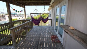 A wooden deck with a railing, two hanging hammocks, and a view of a parking lot and greenery. - In The Heart of Hatteras Village. Close to Beach, Restaurants and Marinas. (Hatteras)