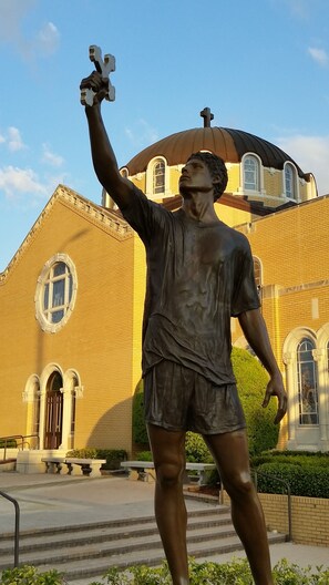 A statue of a man holding a trophy in front of a building with a dome and arched windows.