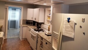 Una cocina compacta con gabinetes blancos, estufa, microondas y refrigerador.