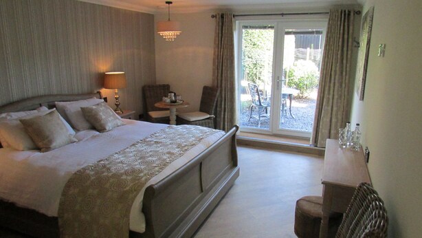 Habitación de hotel con una cama grande, una mesita, una silla y vistas a través de puertas de cristal.
