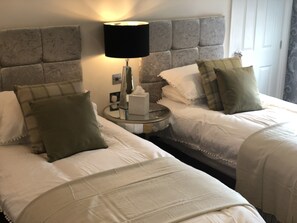 Una camera d'albergo con due letti, un comodino con una lampada e una finestra con tende.