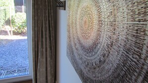 Una habitación con una gran obra de arte mural con textura, una ventana con cortinas y un pequeño adorno en la pared.