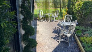 Un patio al aire libre con una mesa y sillas, rodeado por un camino de grava y una cerca de metal.