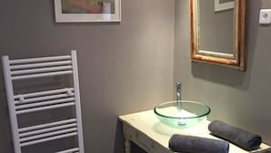 Une salle de bain avec un meuble-lavabo blanc, un lavabo en verre, deux serviettes, un porte-serviettes blanc et un tableau encadré au mur.