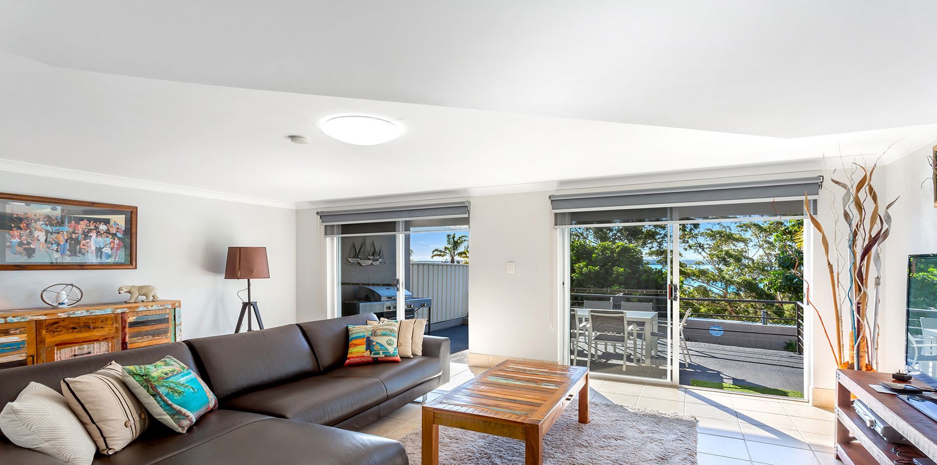 A modern living room with a leather sofa, a coffee table, and a view of a balcony with outdoor furniture.