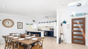 A modern kitchen with white cabinets, a central island, and a dining area with a wooden table and chairs. - Water Views on Wallawa - Gorgeous Nelson Bay Water Views (Nelson Bay)