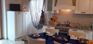 A modern kitchen with white cabinets, a dining table set with blue tablecloth, and a striped curtain.