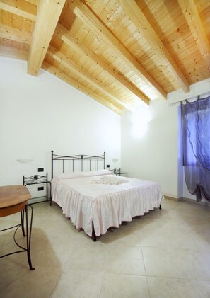 A bedroom with a wooden ceiling, a bed with a white bedspread, a nightstand, and a table.