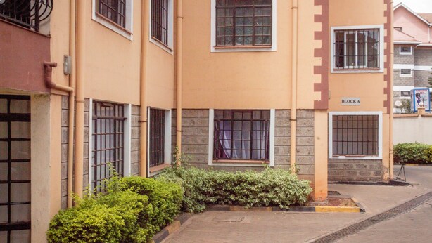 A multi-story building with a beige facade, multiple windows with metal bars, and a sign indicating 'BLOCK A'. - Lomu Homes Kilimani (Nairobi)