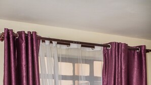 A room with a bed, purple curtains, and a window with a view of buildings. - Lomu Homes Kilimani (Nairobi)