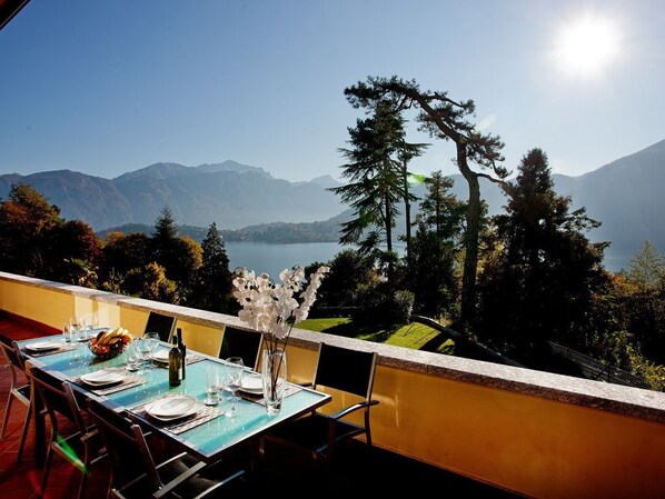 An outdoor dining area with a table set for two, overlooking a lake and mountains. - Tremezzo residence apartment no 11 with pool and spa by Italian Apartments (tremezzo)