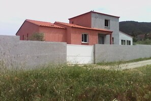 Situated in a serene rural setting, this two-story residence features a red-tiled roof and a white lower section.
