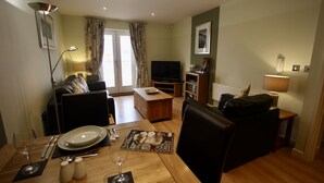 A living room with a dining table set for two, a sofa, a TV, and a lamp. - City Centre Skeldergate 1 Bed Apartment With Parking (York)