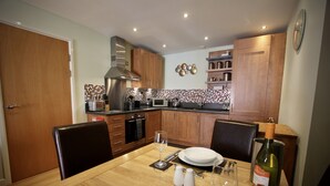 A modern kitchen with wooden cabinets, a microwave, and a dining table set for two. - City Centre Skeldergate 1 Bed Apartment With Parking (York)