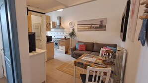 Un espacio habitable compacto con kitchenette, un área de comedor con mesa y sillas, y un sofá con cojines.