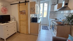 Un espacio habitable compacto con kitchenette, un televisor en una cómoda y una puerta corrediza que da a un balcón.