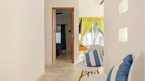 Une pièce avec une chaise blanche, un coussin bleu et blanc, et une porte qui donne sur une autre pièce.