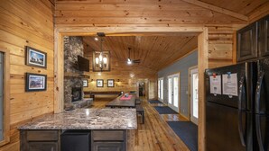 A wooden interior with a kitchen area featuring granite countertops, a stone fireplace, and a black refrigerator.
