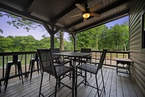 Une terrasse extérieure couverte, dotée d’une table et de chaises, qui offre une vue sur un plan d’eau et des arbres.