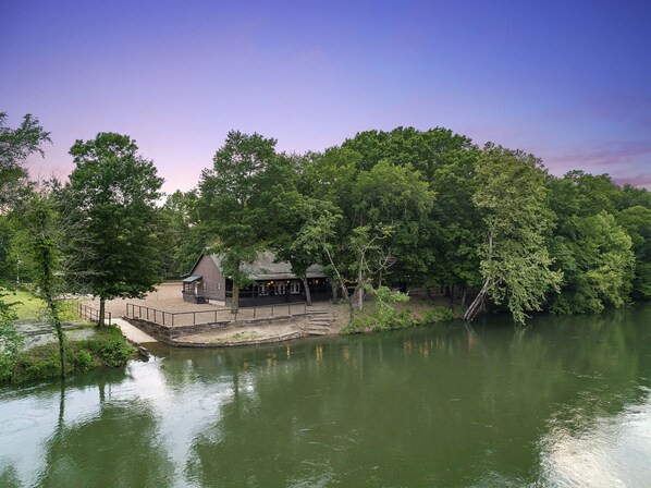Un chalet au bord du lac, doté d’un quai, entouré d’une forêt dense et surplombant un ciel dégagé.