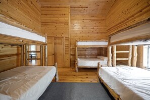 Une cabine équipée de trois lits superposés en bois, d’une porte en bois et d’une petite table avec des chaises.
