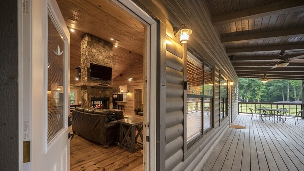 A log cabin with a wooden deck, a stone fireplace, and a cozy living area with a sofa and coffee table.